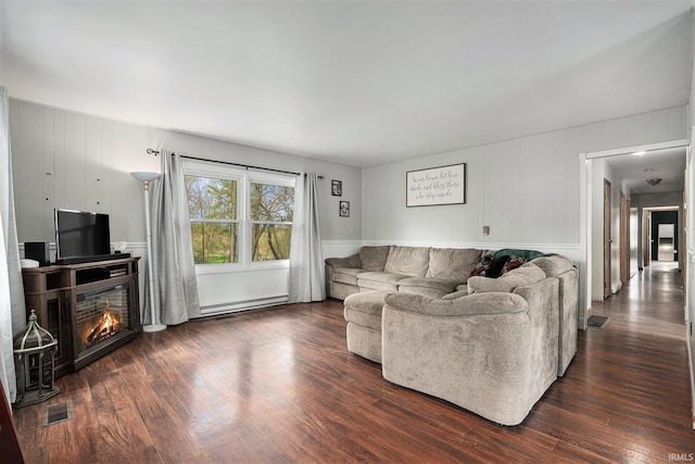 living room with dark wood-style flooring, a glass covered fireplace, visible vents, and a baseboard heating unit