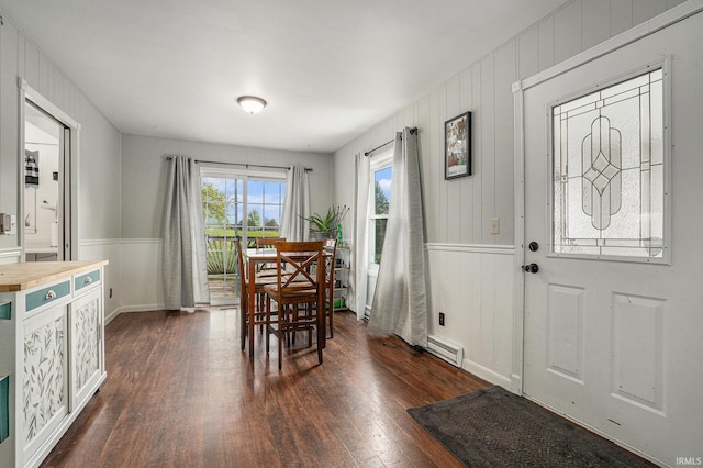 dining room with wainscoting, a baseboard radiator, wood walls, and dark wood finished floors