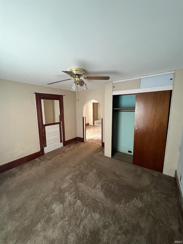 unfurnished bedroom featuring a closet, carpet floors, arched walkways, a ceiling fan, and baseboards
