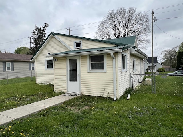 back of house featuring metal roof, fence, and a lawn