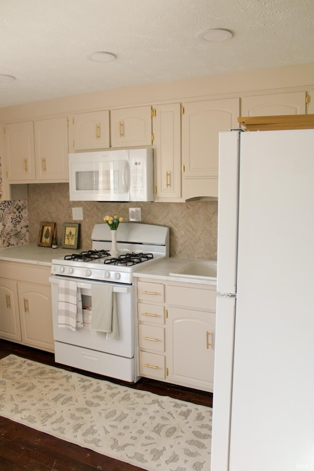 kitchen featuring a sink, white appliances, decorative backsplash, light countertops, and dark wood-style floors