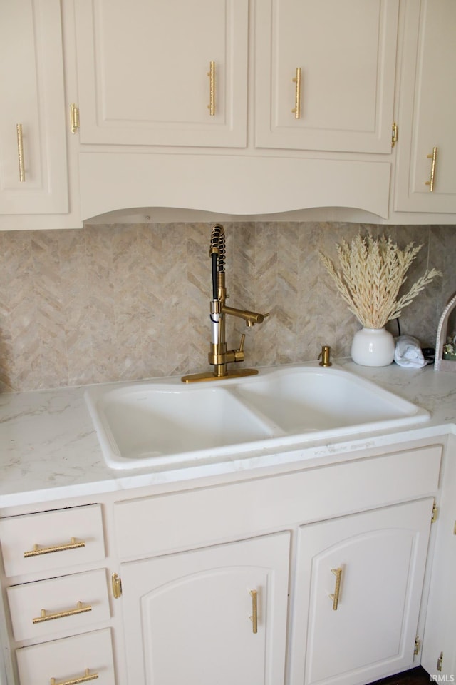 room details with light countertops, decorative backsplash, white cabinets, and a sink