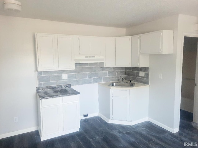2225 S Hoyt Ave, Muncie, IN 47302 - kitchen with a sink, under cabinet range hood, dark wood-style flooring, white cabinets, and baseboards