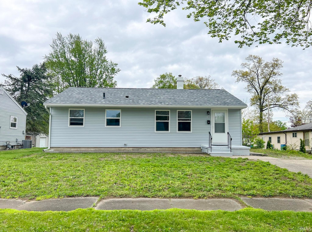view of front of house with central AC unit, roof with shingles, a chimney, and a front yard