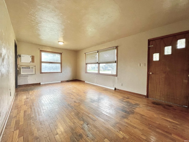 unfurnished living room with baseboards, baseboard heating, plenty of natural light, and hardwood / wood-style flooring