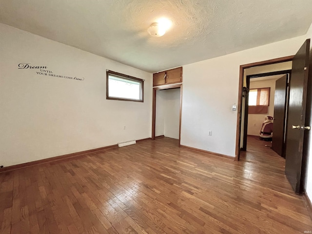 unfurnished bedroom featuring a closet, a textured ceiling, baseboards, visible vents, and hardwood / wood-style flooring