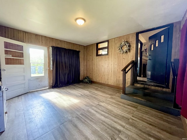 unfurnished living room featuring wood finished floors, wood walls, and baseboards