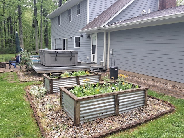 exterior space with a hot tub, a wooden deck, a shingled roof, and a vegetable garden