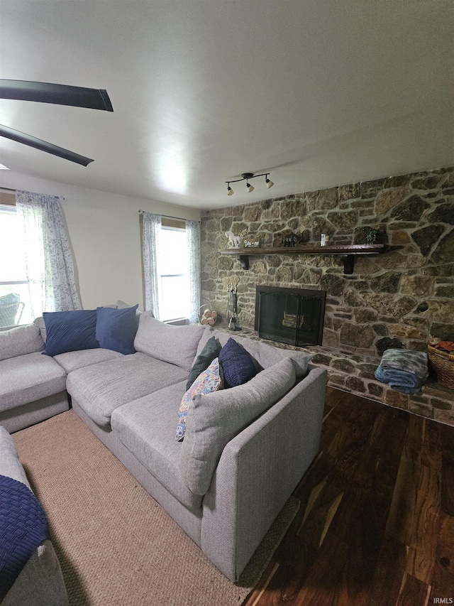 living room featuring a stone fireplace, track lighting, and wood finished floors