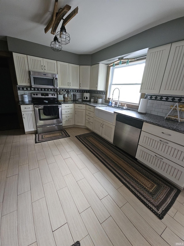 kitchen featuring stainless steel appliances, decorative backsplash, a sink, dark countertops, and light wood-type flooring