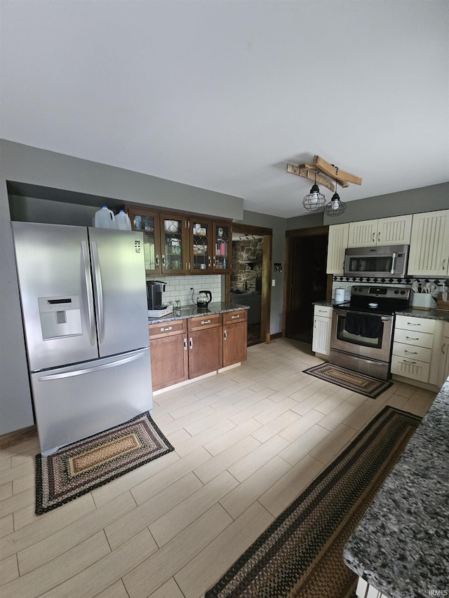 kitchen with decorative backsplash, dark stone countertops, glass insert cabinets, and appliances with stainless steel finishes