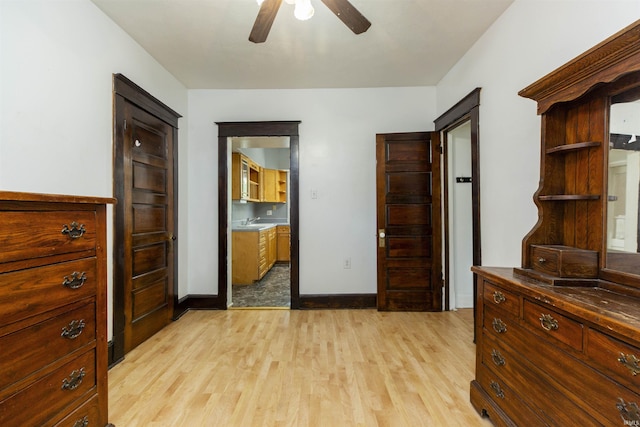 bedroom featuring light wood finished floors, a sink, baseboards, ceiling fan, and ensuite bath