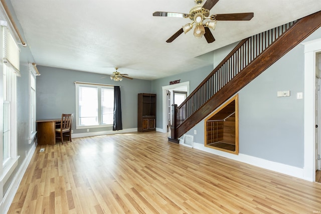 unfurnished living room with baseboards, stairs, light wood-style floors, and ceiling fan