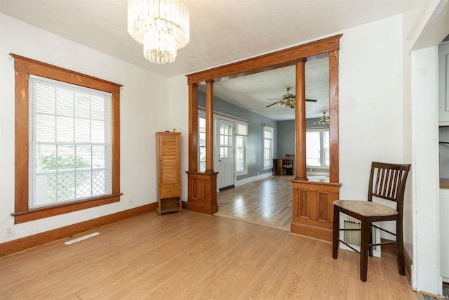 interior space featuring ceiling fan with notable chandelier, baseboards, light wood-type flooring, and ornate columns