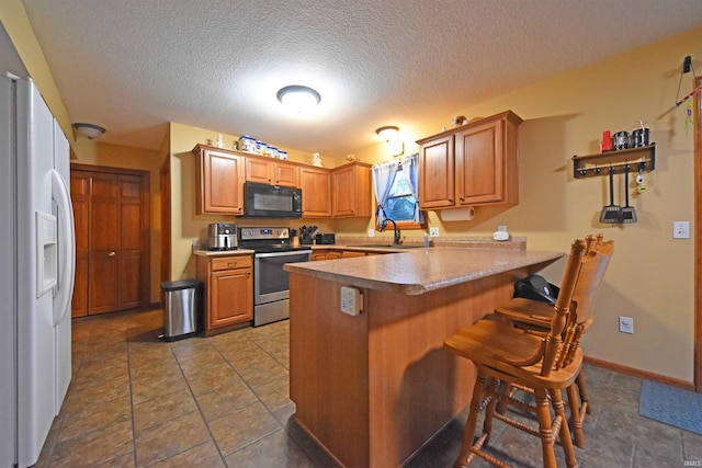 kitchen with a peninsula, stainless steel range with electric stovetop, a breakfast bar area, white fridge with ice dispenser, and black microwave
