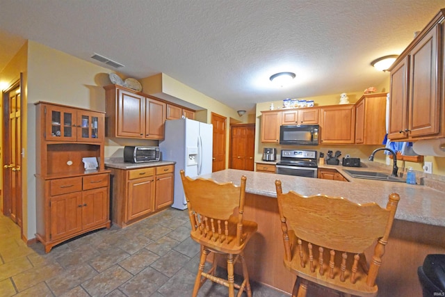 kitchen with a sink, stainless steel range with electric stovetop, visible vents, black microwave, and white refrigerator with ice dispenser