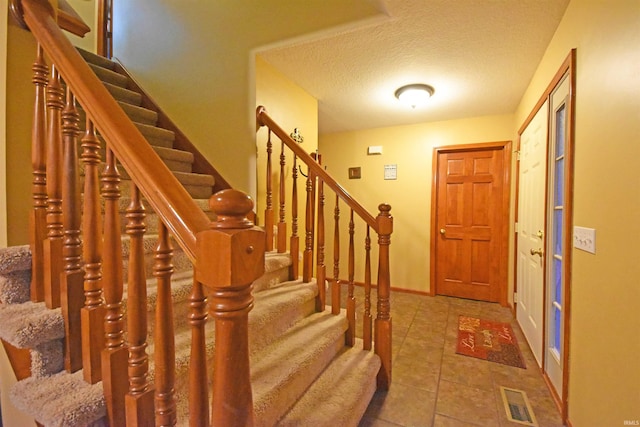 tiled entrance foyer with stairway, a textured ceiling, baseboards, and visible vents