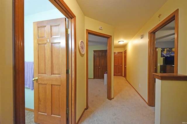 hall featuring baseboards and light carpet
