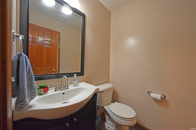 half bath with toilet, baseboards, and vanity