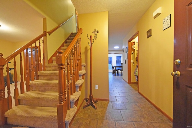 staircase with a textured ceiling, baseboards, and tile patterned floors