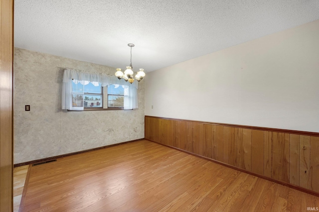 unfurnished room featuring a chandelier, light wood-style floors, a wainscoted wall, and a textured ceiling