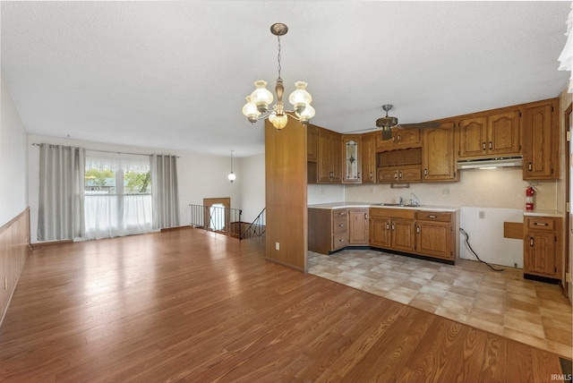 kitchen featuring a chandelier, brown cabinetry, under cabinet range hood, light countertops, and light wood finished floors