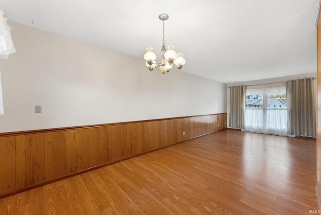 spare room with wood finished floors, a chandelier, wainscoting, and wood walls
