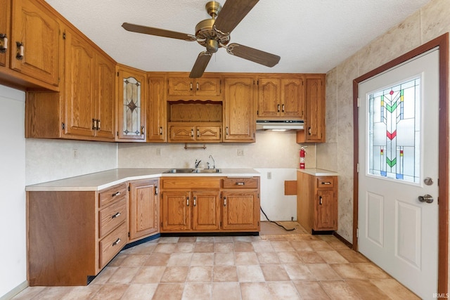 kitchen with under cabinet range hood, a sink, brown cabinetry, ceiling fan, and light countertops