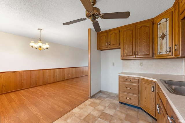 kitchen featuring brown cabinetry, ceiling fan, light countertops, a chandelier, and decorative light fixtures