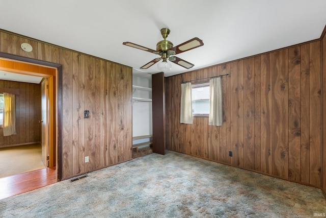 carpeted empty room featuring a ceiling fan, wooden walls, and a smoke detector