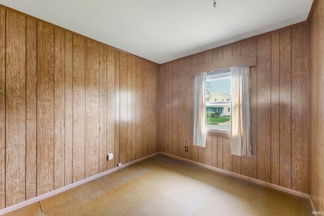 empty room with wood walls, baseboards, and carpet