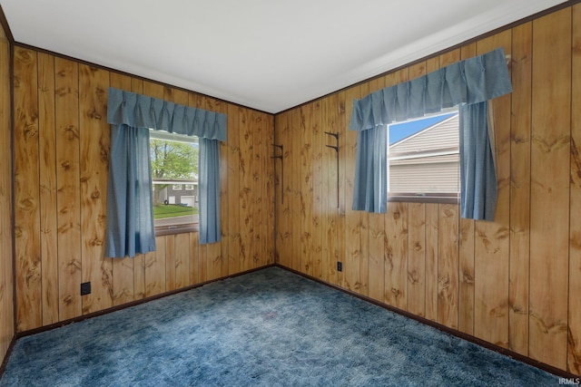 empty room featuring dark colored carpet, wood walls, and baseboards