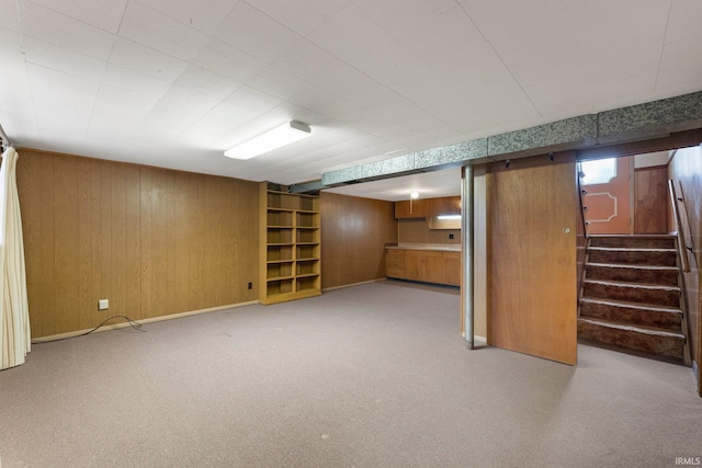 below grade area featuring wooden walls, stairway, light carpet, and baseboards