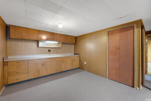 kitchen with carpet flooring, wood walls, light countertops, and brown cabinetry
