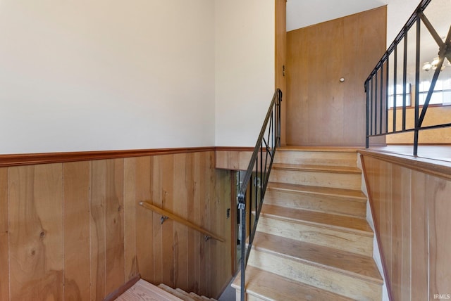 stairway with a wainscoted wall and wood walls