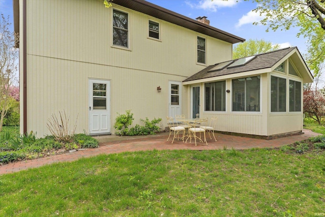 back of house with a sunroom, a patio, a chimney, and a yard