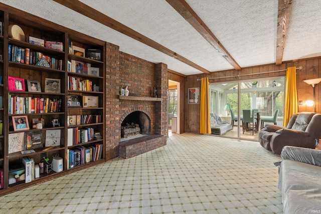 living area with wooden walls, a textured ceiling, beam ceiling, a brick fireplace, and carpet