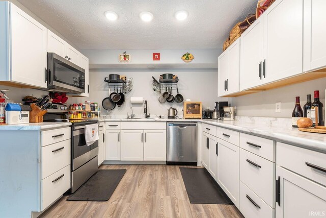 4346 N Centennial Dr, Bloomington, IN 47404 - kitchen with appliances with stainless steel finishes, a sink, light wood-style floors, white cabinetry, and a textured ceiling