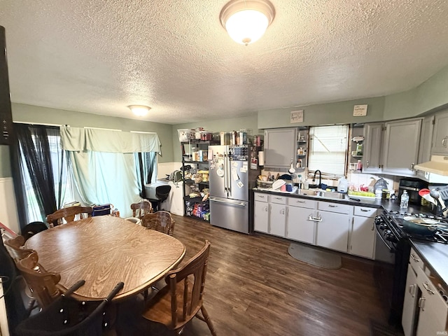 kitchen featuring freestanding refrigerator, a textured ceiling, a sink, range hood, and dark countertops