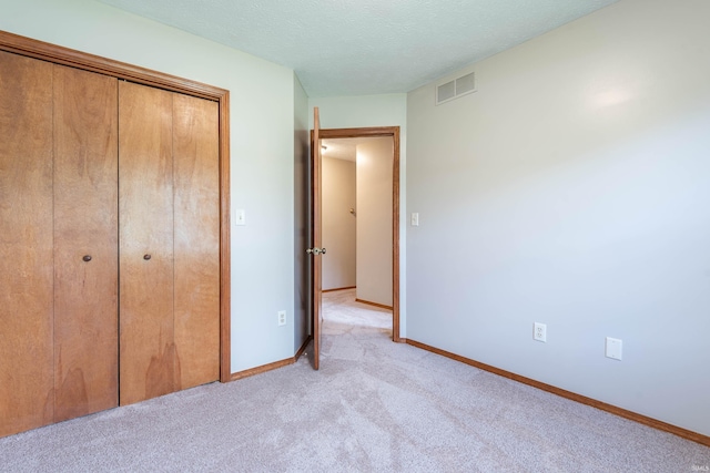 unfurnished bedroom featuring light carpet, a closet, baseboards, and a textured ceiling
