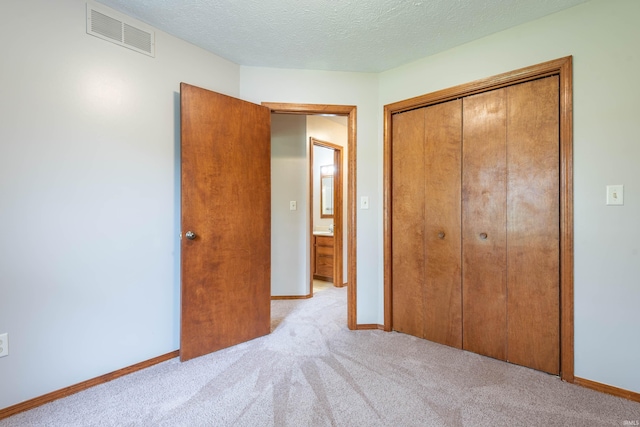 unfurnished bedroom with light carpet, a closet, baseboards, and a textured ceiling