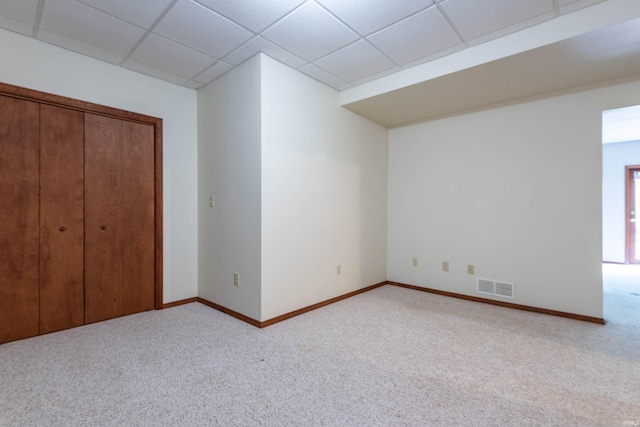 unfurnished bedroom featuring carpet, baseboards, a drop ceiling, and a closet
