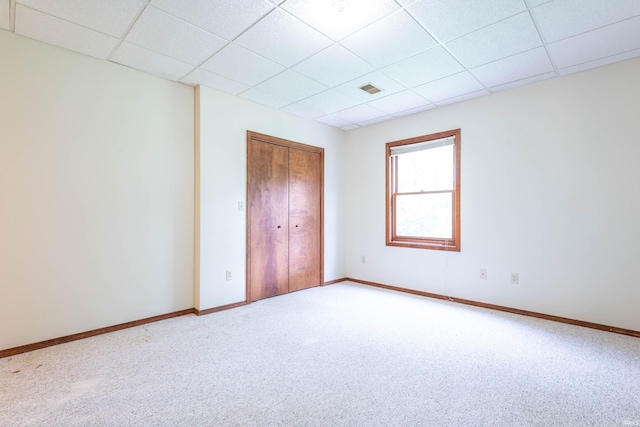 unfurnished bedroom with a drop ceiling, carpet floors, baseboards, and a closet