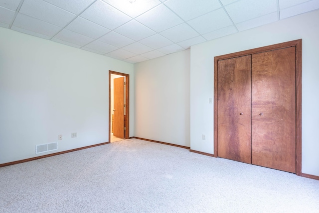 unfurnished bedroom featuring a drop ceiling, carpet floors, baseboards, and a closet