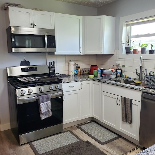 1202 Magnolia Ave, Frankfort, IN 46401 - kitchen featuring stainless steel appliances, backsplash, white cabinetry, and light wood finished floors