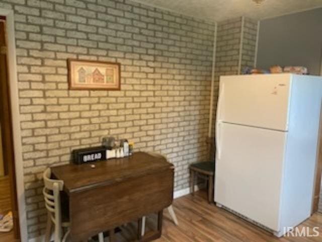 kitchen with freestanding refrigerator, wood finished floors, and brick wall
