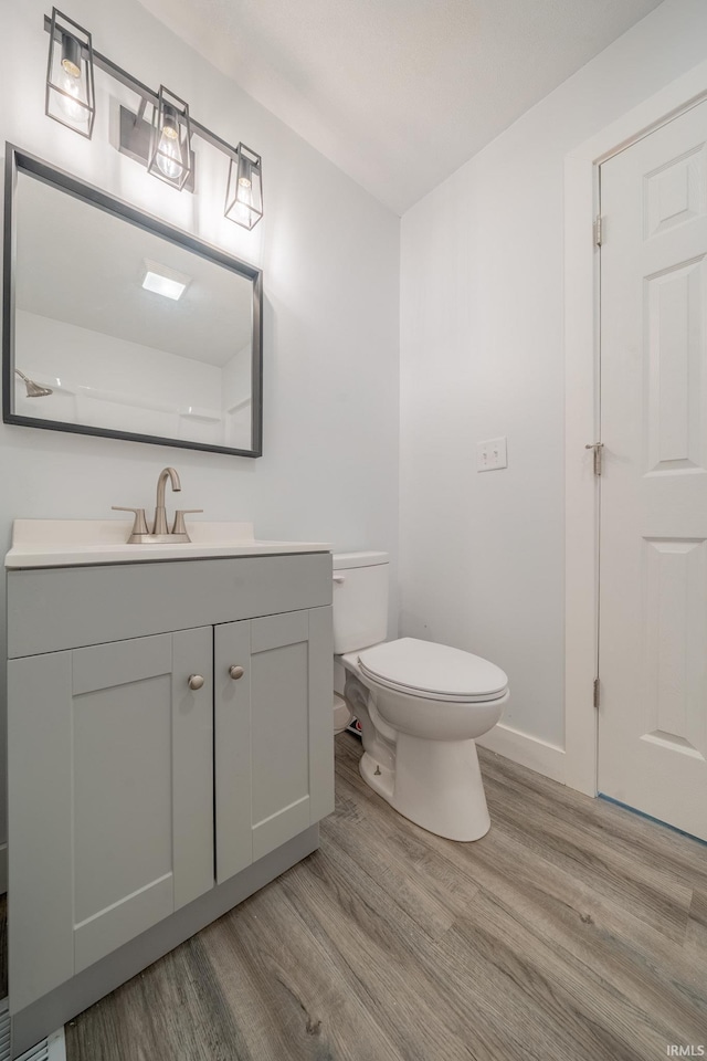 half bath featuring wood finished floors, toilet, vanity, and baseboards