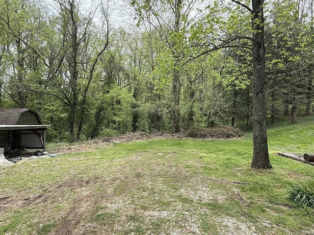 view of green lawn featuring an outbuilding, a storage unit, and a wooded view
