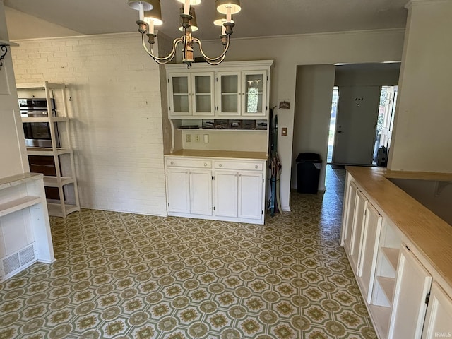 kitchen with brick wall, a chandelier, glass insert cabinets, white cabinetry, and light countertops