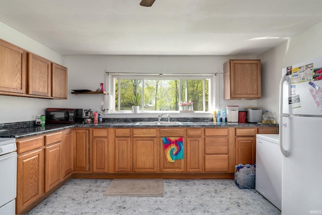 kitchen with freestanding refrigerator, a sink, black microwave, brown cabinetry, and stove